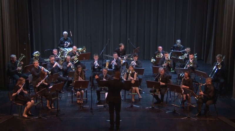 Na scenie grają muzycy z orkiestry, przed nimi stoi dyrygent