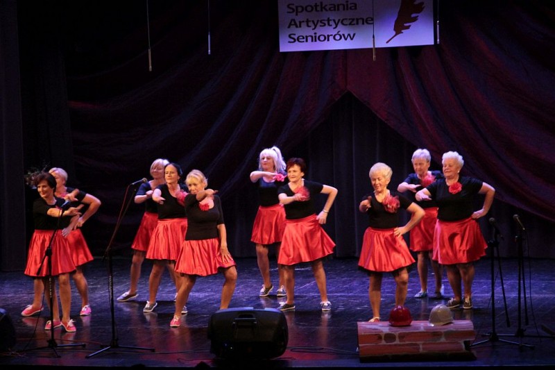 Kobiety tańczą na scenie. Mają czarne koszuli i czerwone spódnice