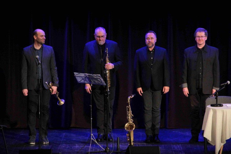 Czterech mężczyzn stoi na scenie trzymając instrumenty muzyczne