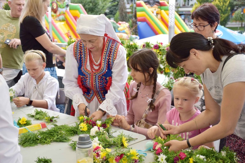 Kobieta w stroju ludowym wraz z dziećmi przygotowuje wiązanki z kwiatów