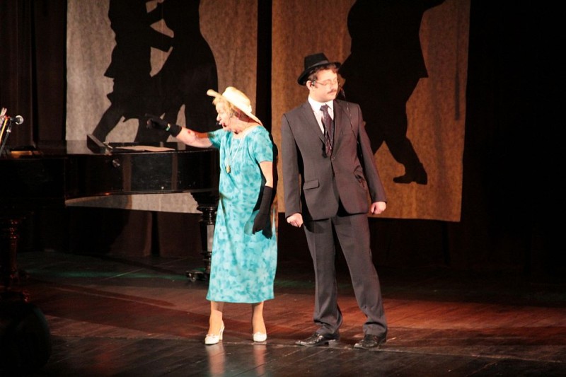 Na scenie mężczyzna w kapeluszu i kobieta w zielonej sukience