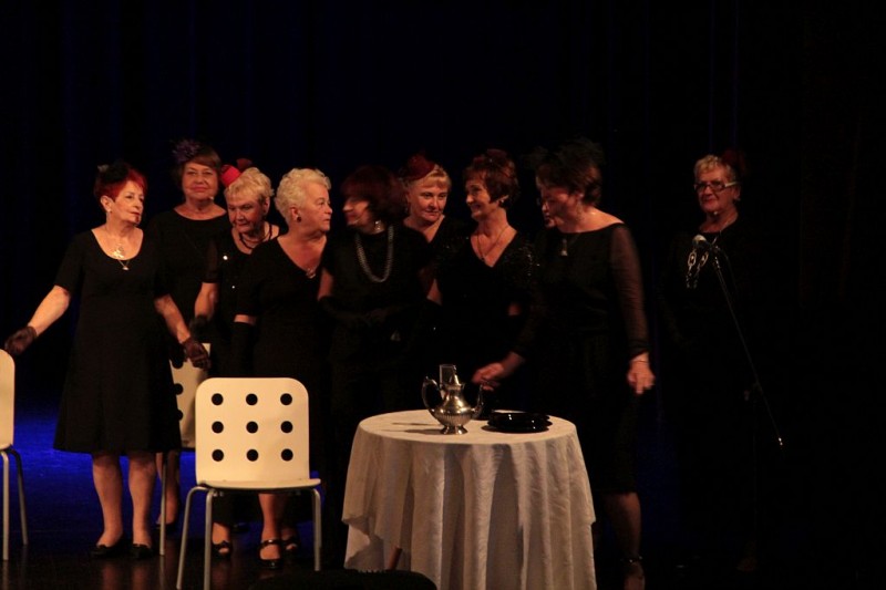Grupa kobiet w czarnych sukienkach stoi przy małym stoliku