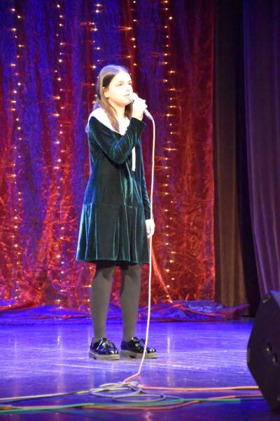 Na scenie śpiewa dziewczynka w ciemno zielonej sukience
