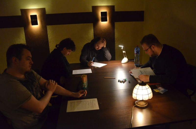 Gracze siedzą przy stole na którym palą się dwie lampki nocne
