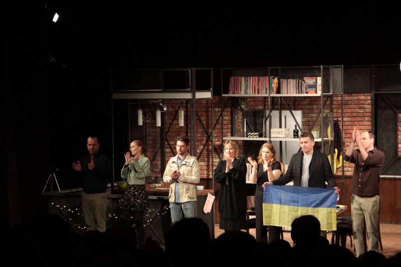 Wszyscy aktorzy stoją razem na scenie, jeden z nich trzyma w rękach flagę Ukrainy