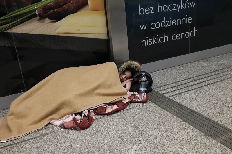 Kobieta okryta kocem śpi na podłodze pod sklepem