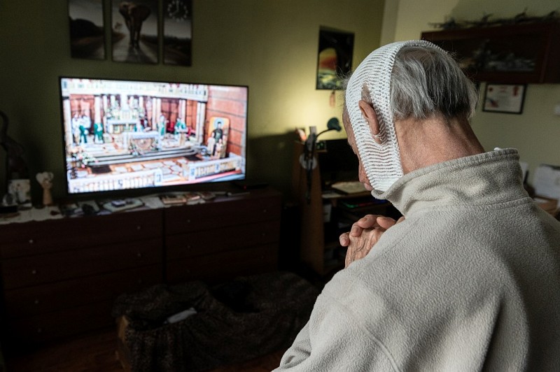 Mężczyzna z bandażem na głowie ogląda telewizje