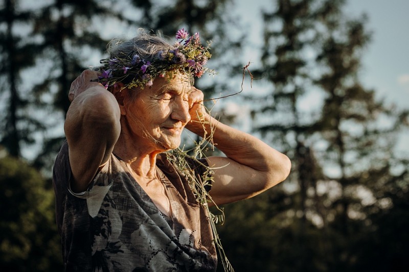 Starsza kobieta z wiankiem z kwiatów polnych na głowie z promieniach zachodzącego słońca