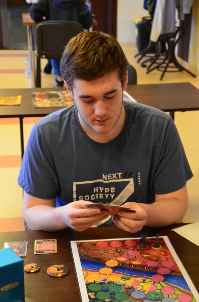 Mężczyzna w szarek koszulce trzyma w rękach karty do gry