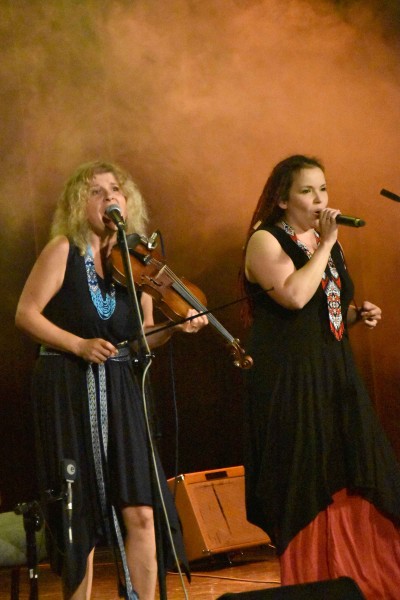 Dwie kobiety na scenie, jedna gra na skrzypach a druga śpiewa