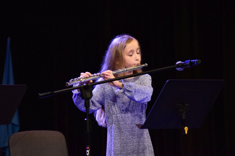 Dziewczynka w niebieskiej sukience gra na flecie poprzecznym