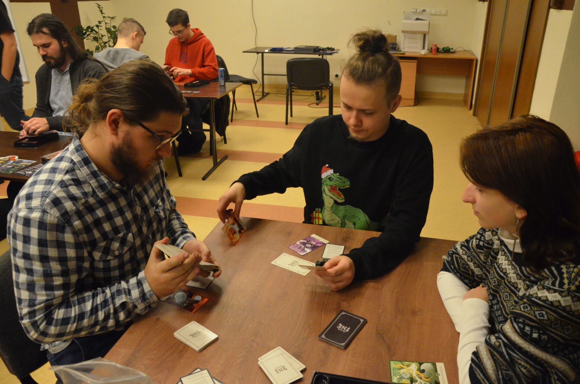 Przy stole trzy osoby grają w grę karcianą "To ja Go Tnę".